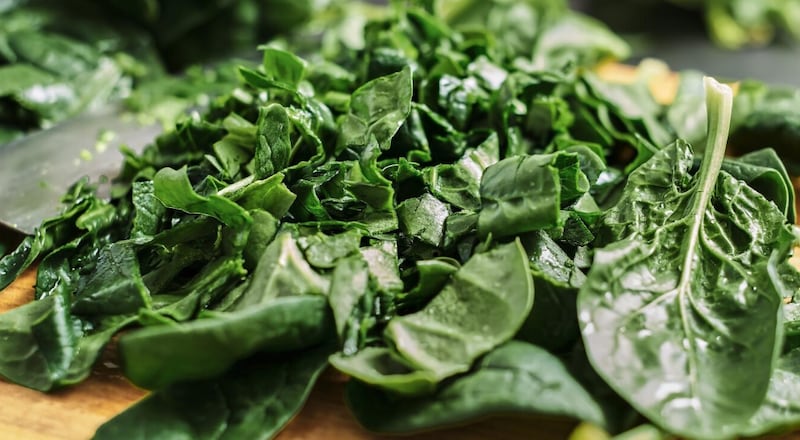 Jugosas hojas de espinaca en rodajas verdes se encuentran sobre una tabla de cortar de madera. Enfoque selectivo, primer plano de espinacas. La idea de preparar el desayuno a partir de alimentos orgánicos saludables.