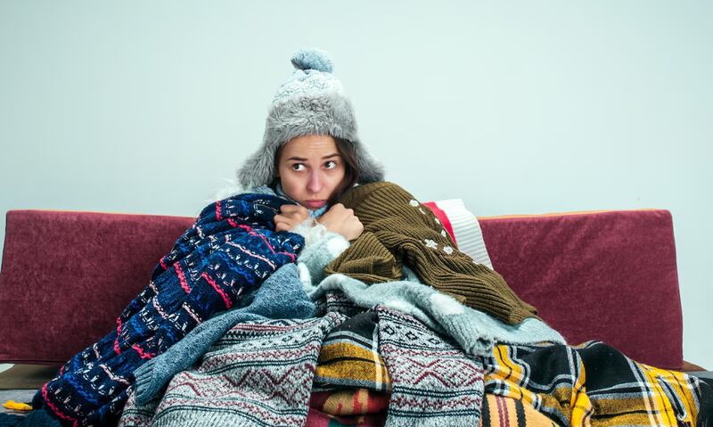 La joven enferma con chimenea sentada en el sofá en casa o estudio cubierto con ropa de abrigo tejida.